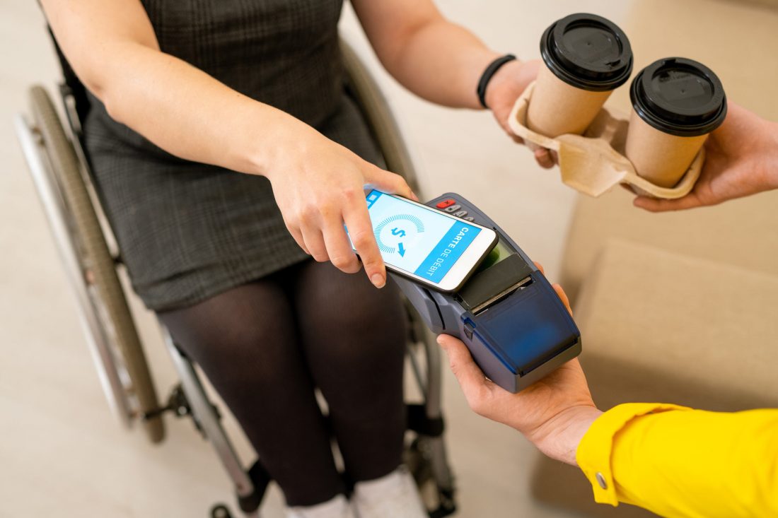 Une femme en chaise roulante paye pour ses cafés à l'aide d'une borne de paiement sans-fil